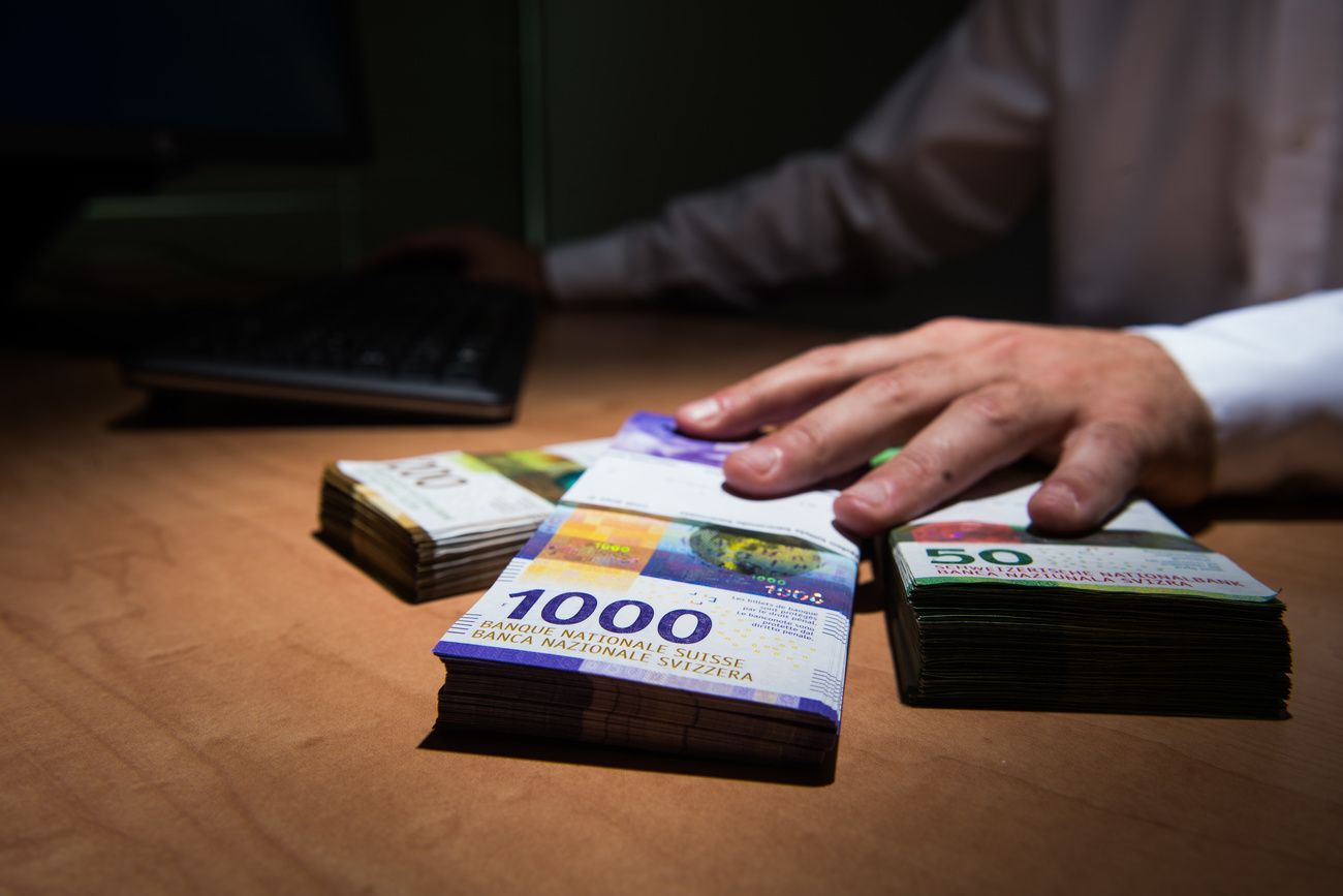 Hand passes bundles of Swiss francs over a desk