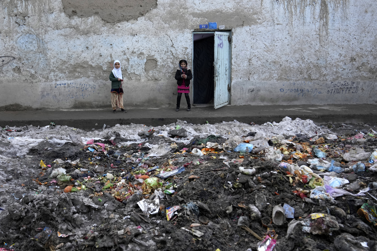 Dos niñas frente a su casa en una calle llena de basura en Kabul