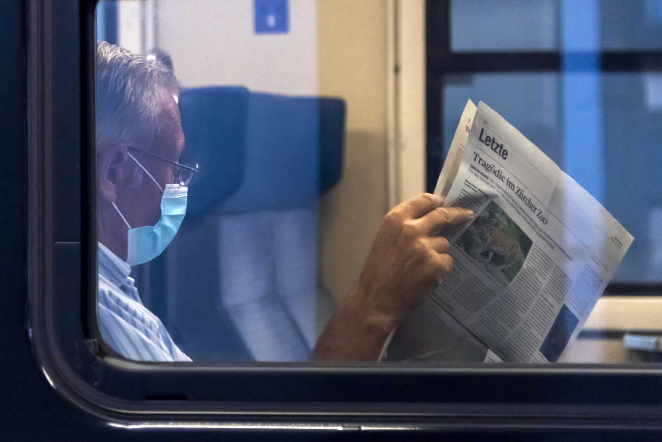 uomo con mascherina legge giornale sul treno