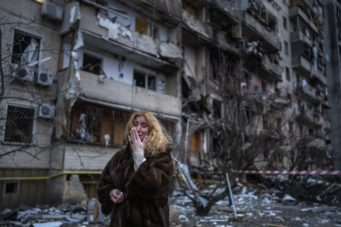 Frau vor verbombten Gebäude in Kiew