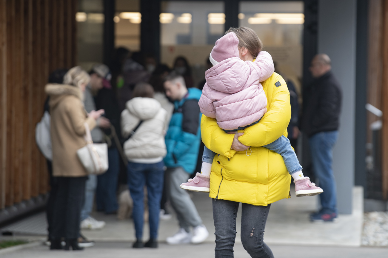 donna con giacca invernale gialla tiene in braccio bambina con ghiacca e berretto rosa