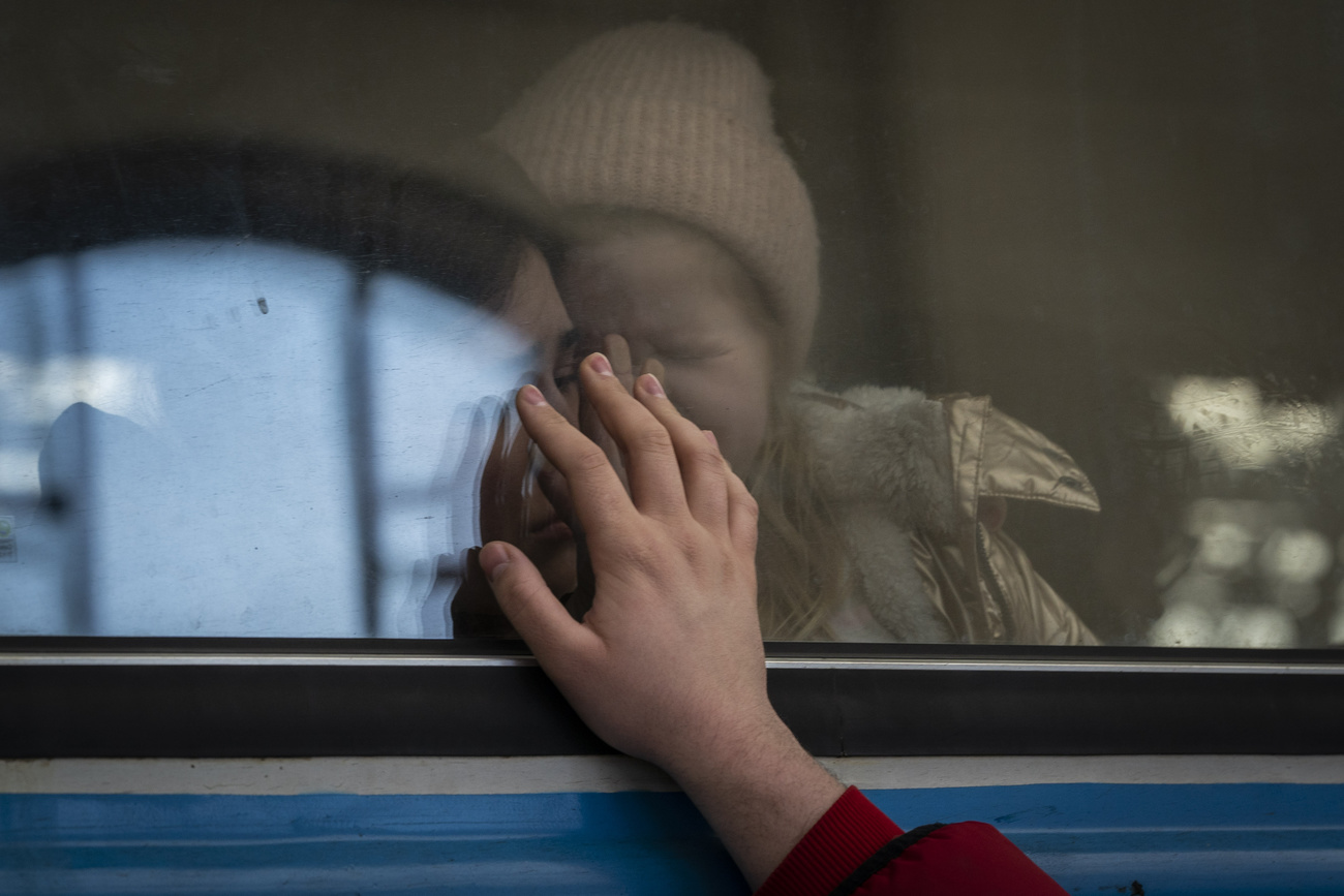 Una mujer con un bebé al interior de un tren y la mano de una persona que se despide desde el exterior