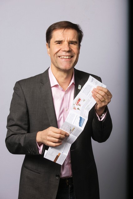Homme posant avec une brochure dans les mains.