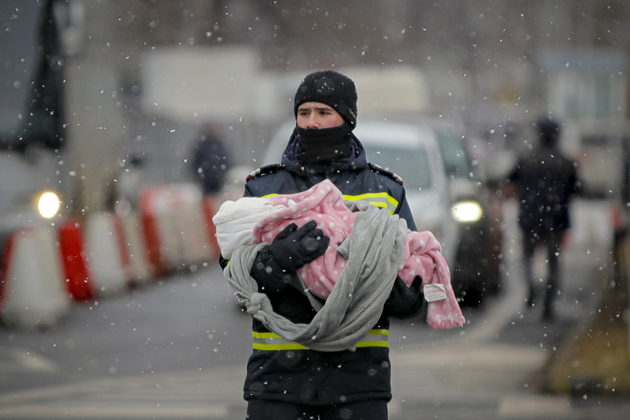Un uomo porta in braccio un neonato sotto la neve che scende.