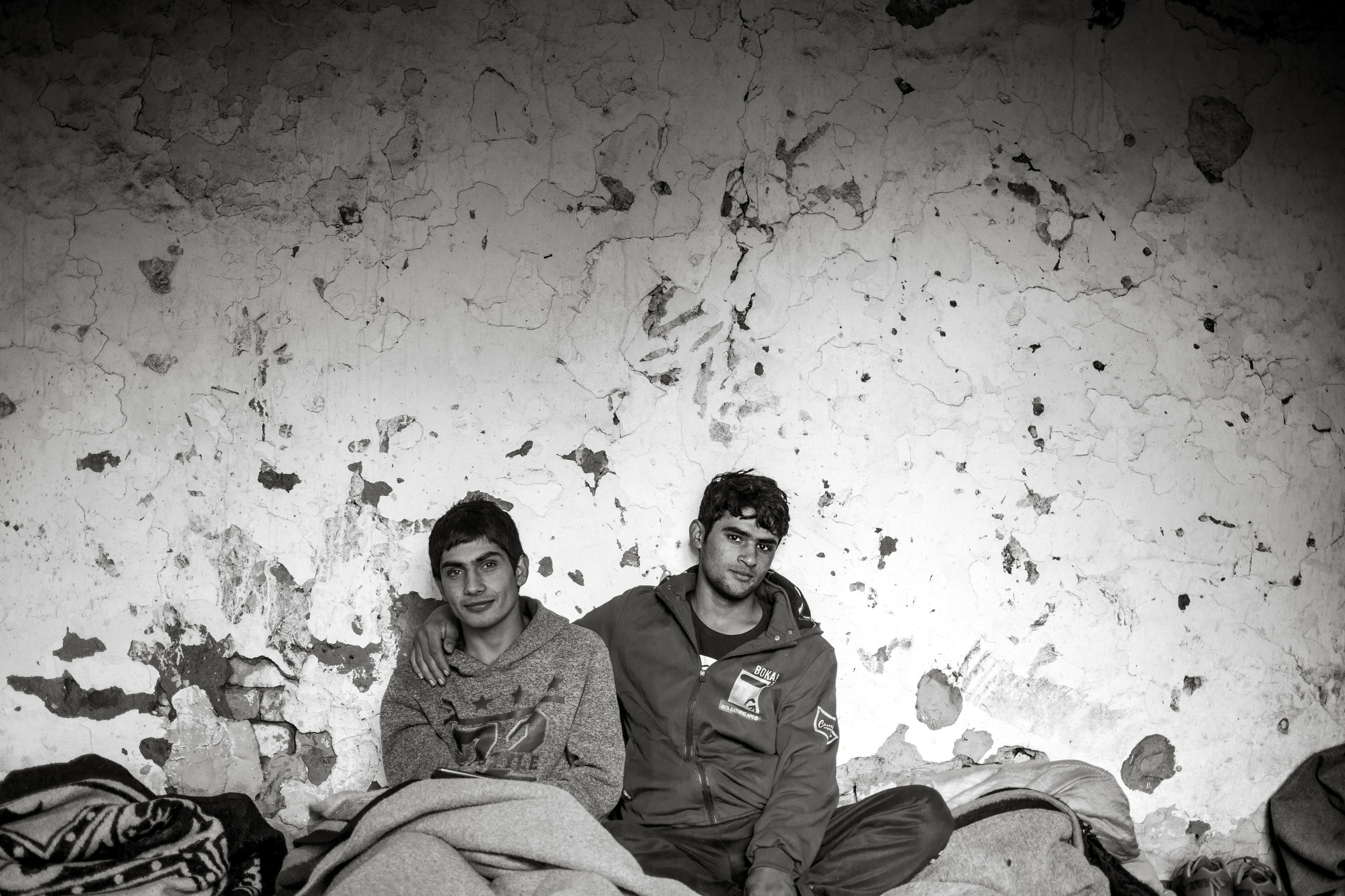 Deux jeunes hommes assis devant un mur en mauvais état