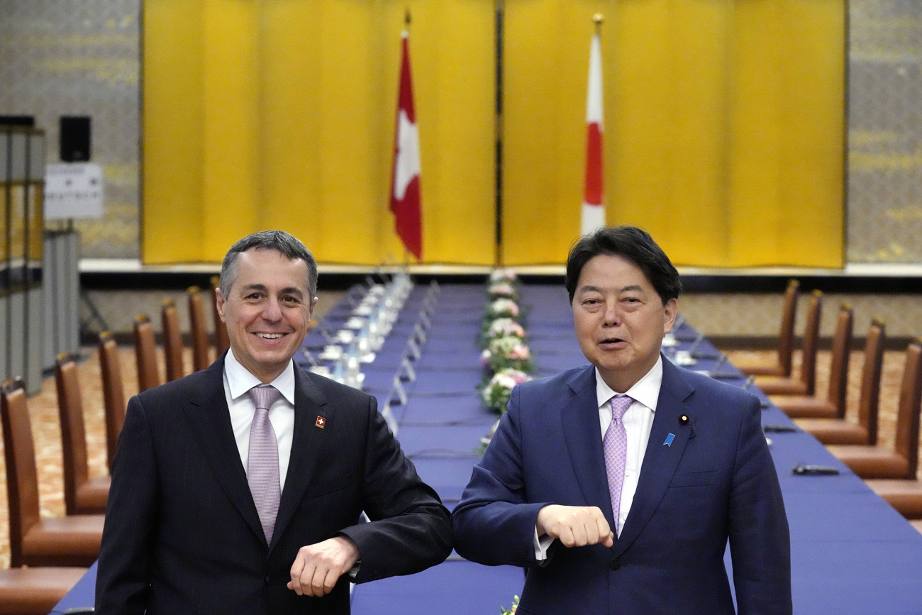 Os Ministros das Relações Exteriores da Suíça (esquerda) e do Japão se cumprimentam com cotovelos
