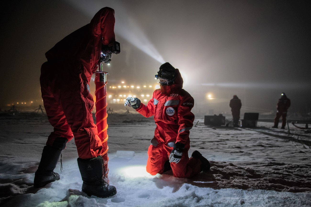 zwei Personen in Winterkleidung bohren mit einem Bohrer ein Loch ins Eis