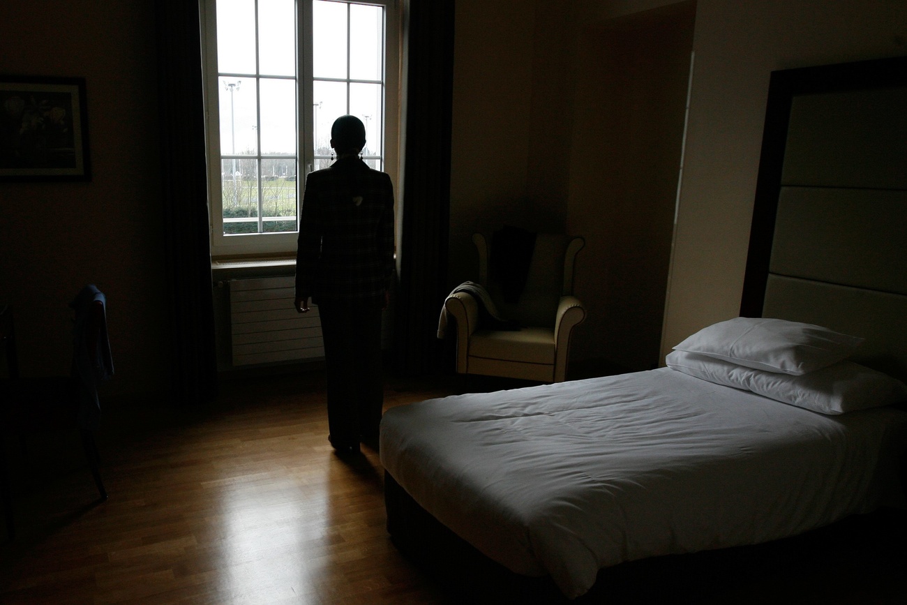 persona fotografata di spalle in pidi accanto a un letto guarda fuori dalla finestra