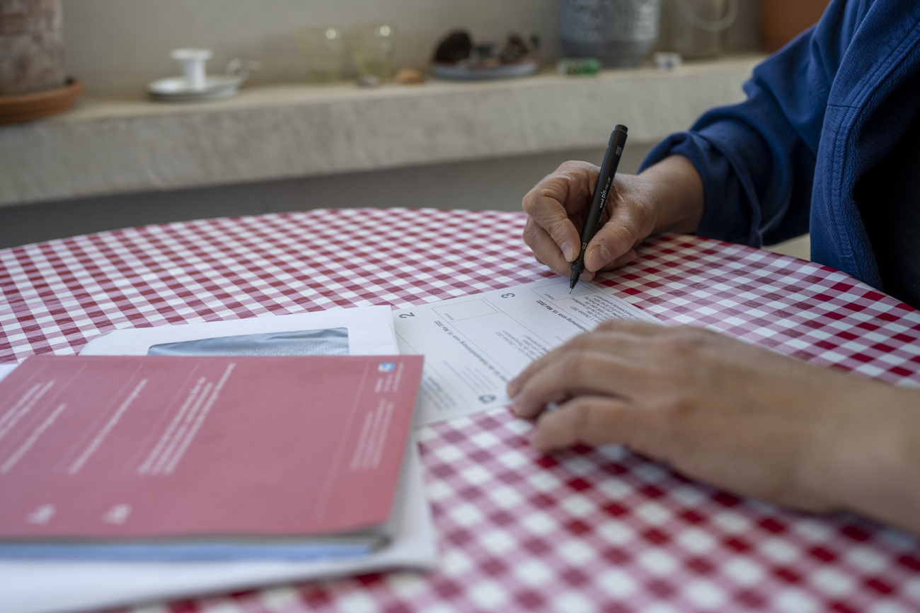 mani in primo piano, una tiene una penna e sta scrivendo qualcosa su una schedina di voto.
