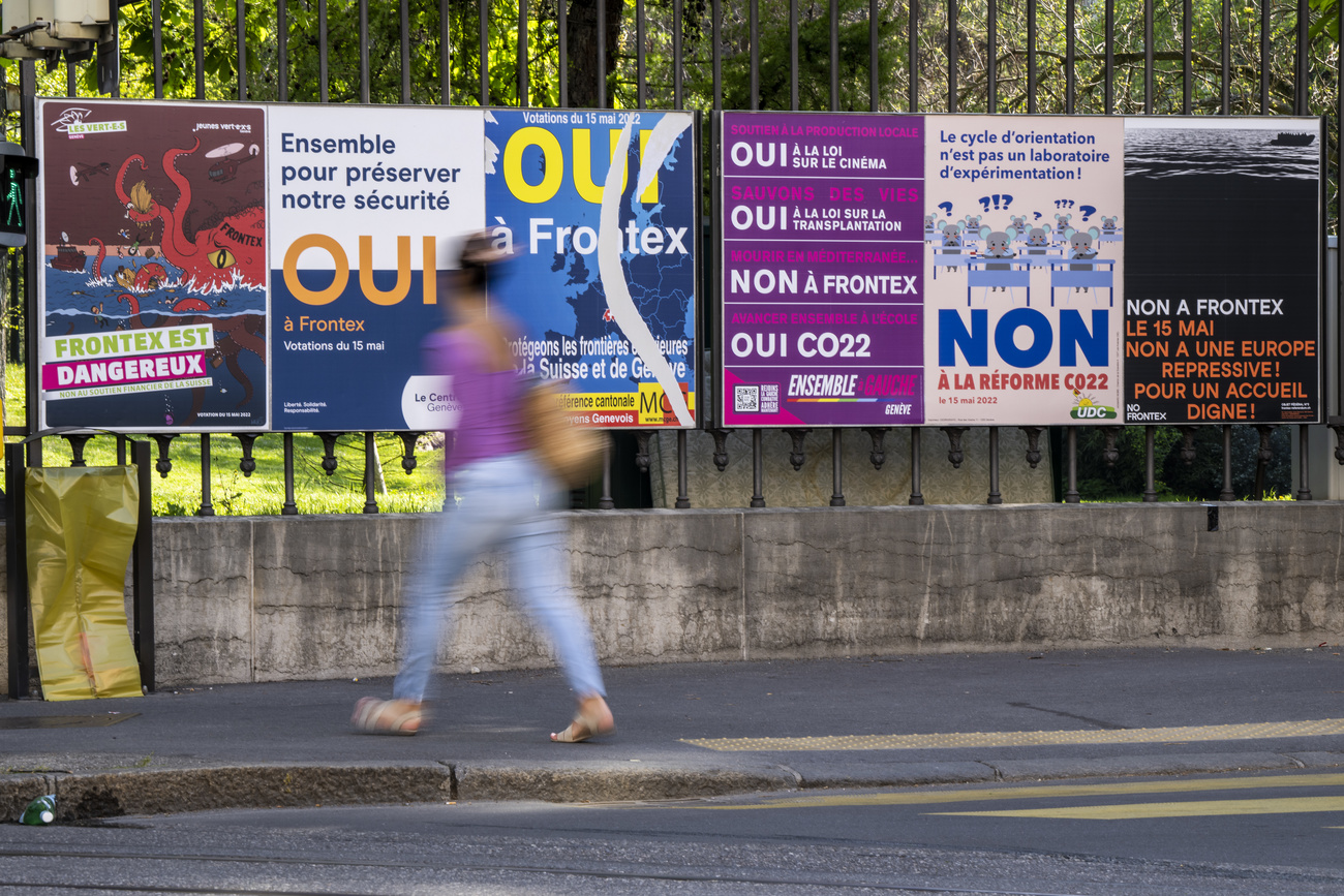 Una mujer caminando frente a pancartas de campaña electoral en relación al tema Frontex