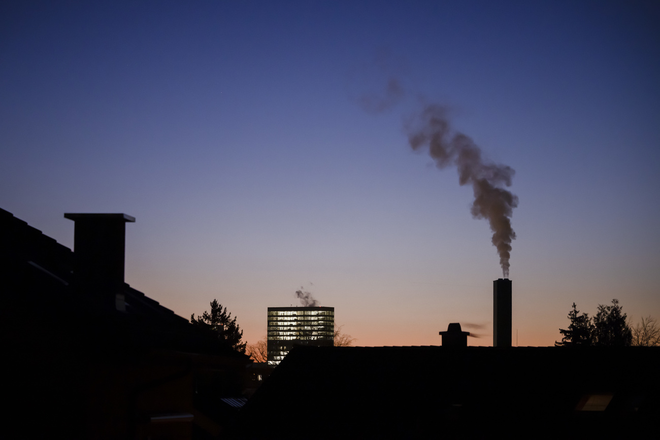 tetti in controluce al tramonto, da una ciminiera esce fumo