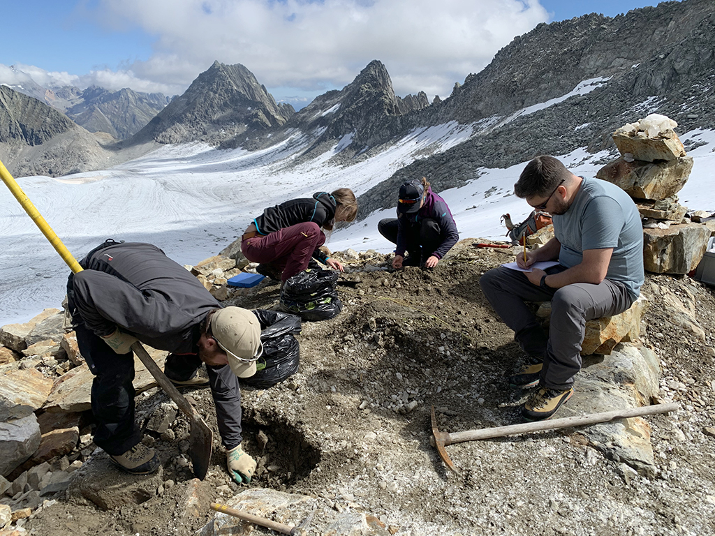 4 people working on a mountain-top archaeology dig