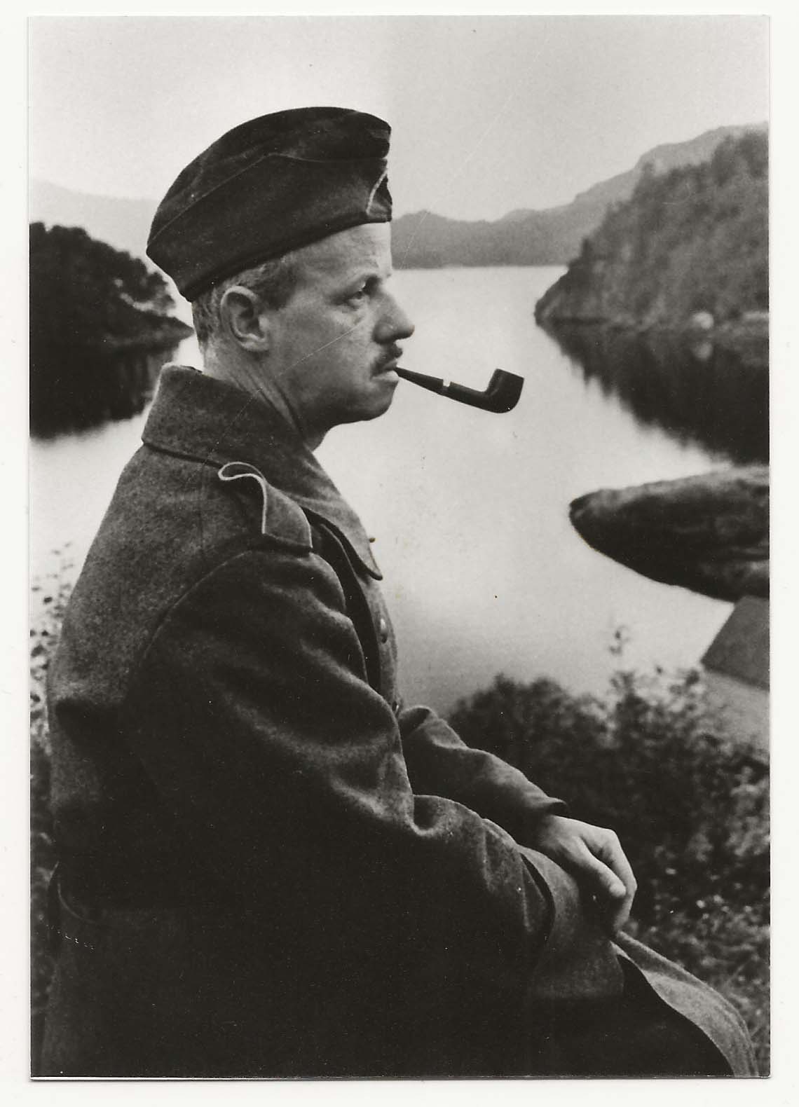 Homme en uniforme allemand fumant la pipe près d un fjord.