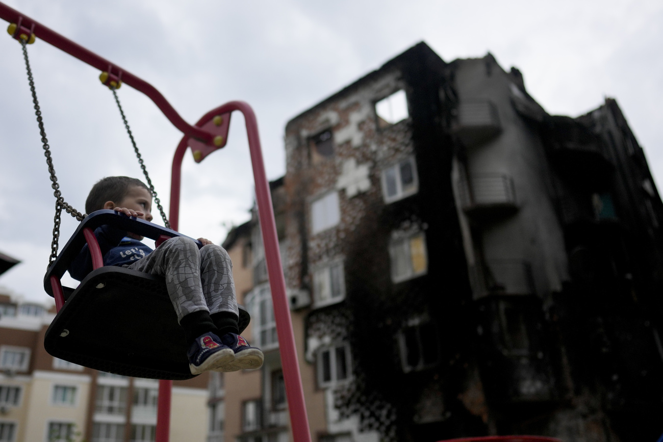 Bambino su altalena davanti alle macerie