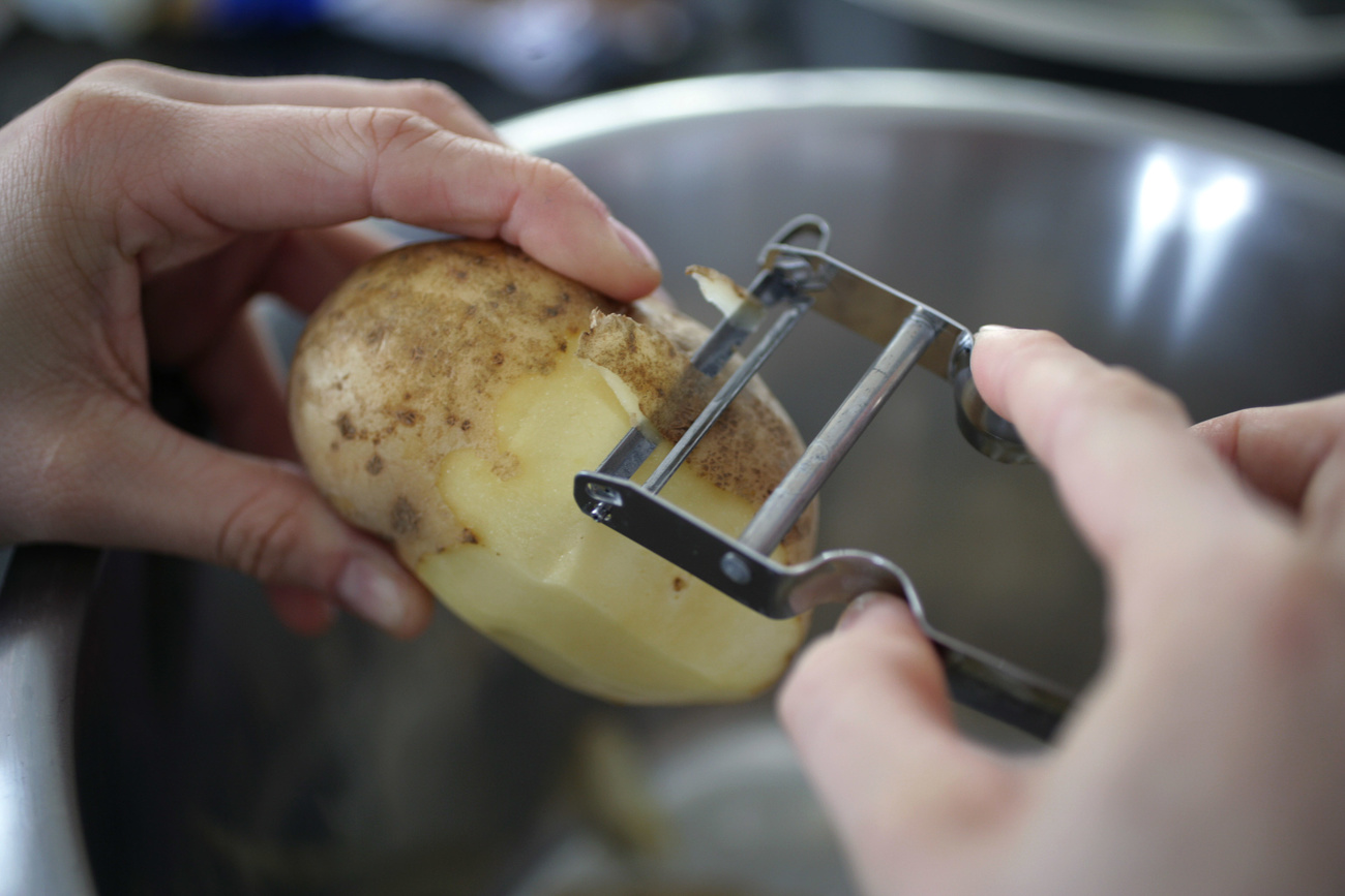 primo piano di mani che pelano una patata con il pelapatate svizzero Rex