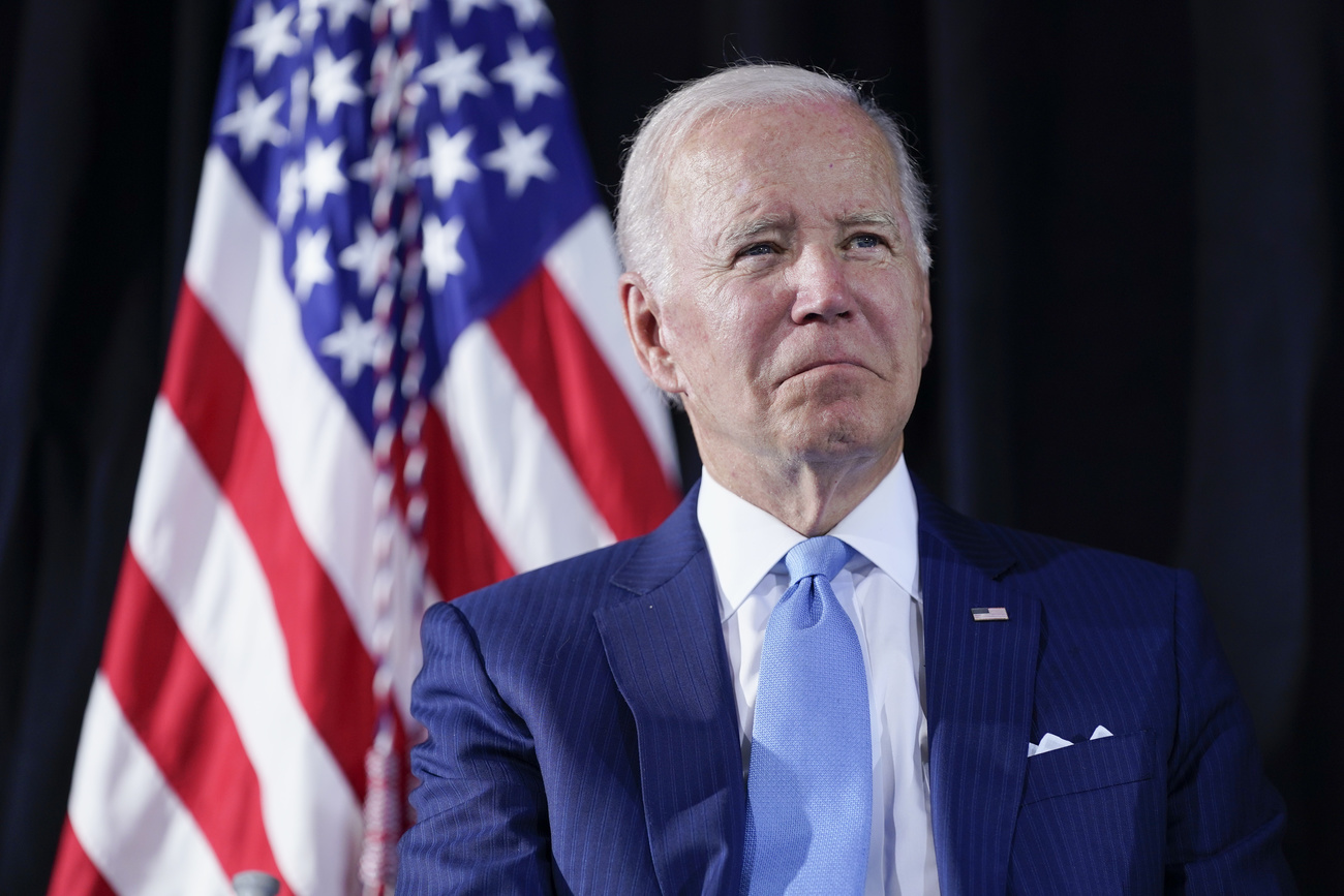 Primo piano di Joe Biden, con bandiera americana alle spalle.