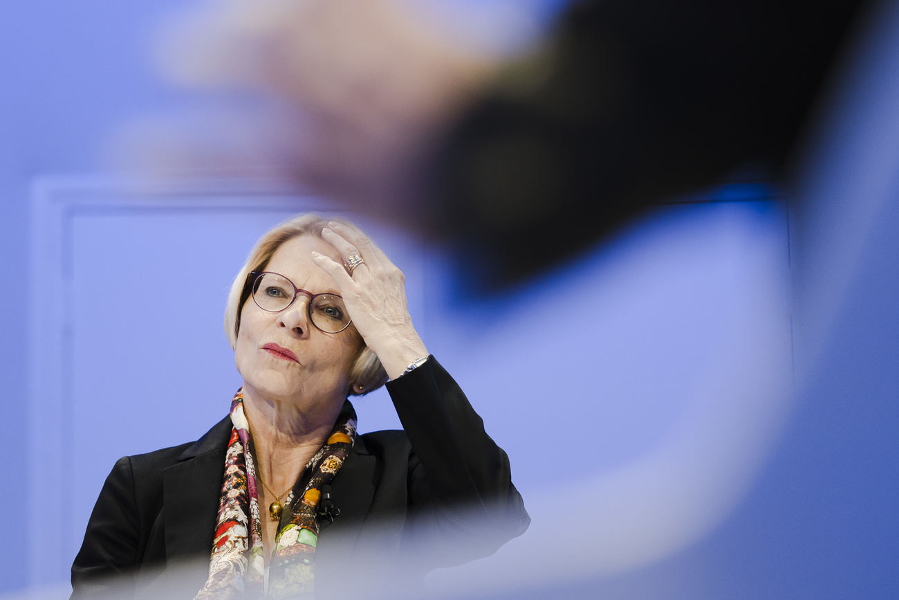 mezzo busto di donna bionda con occhiali e rossetto rosso che si aggiusta i capeli con la mano sinistra