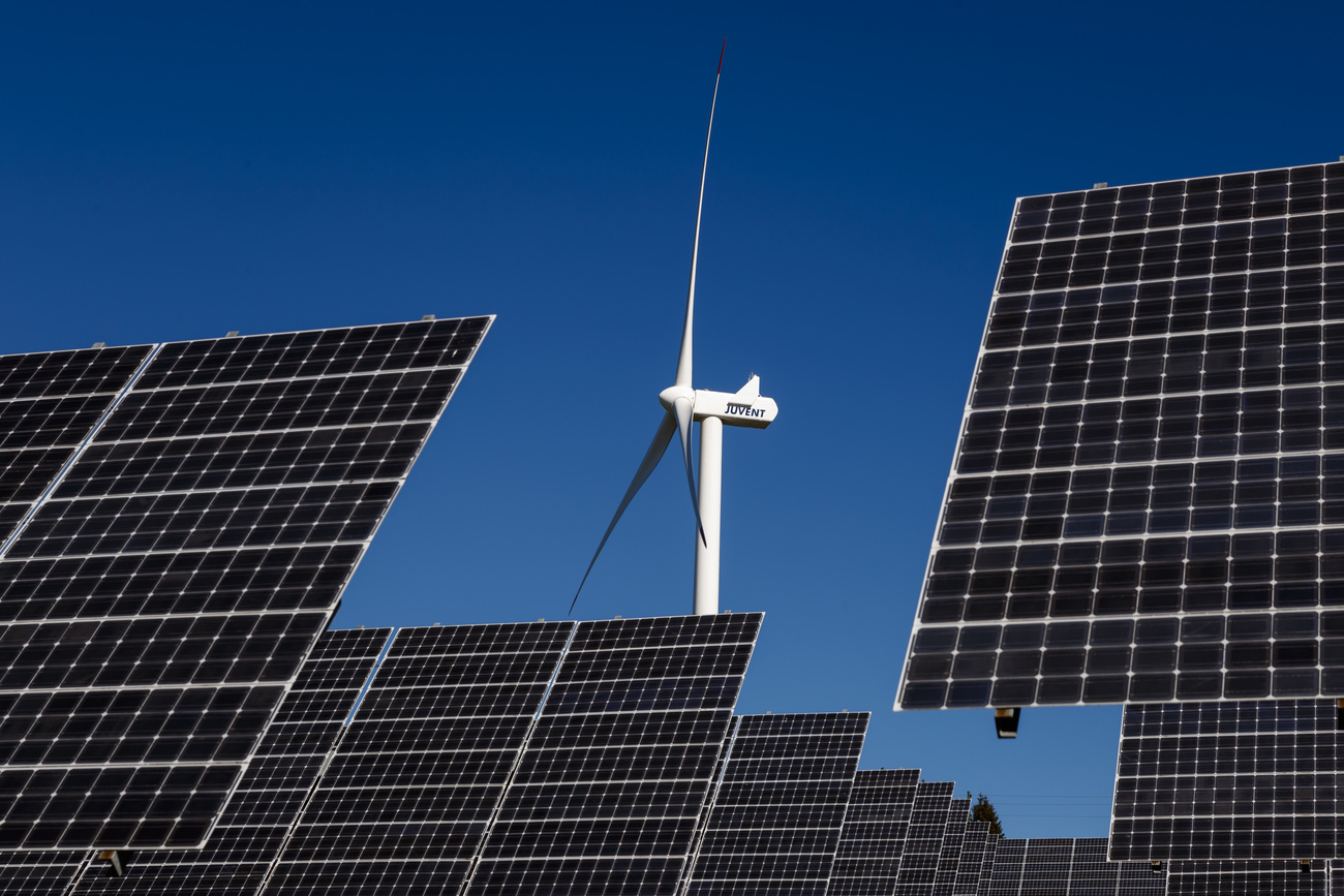 wind turbine stands behind solar panels