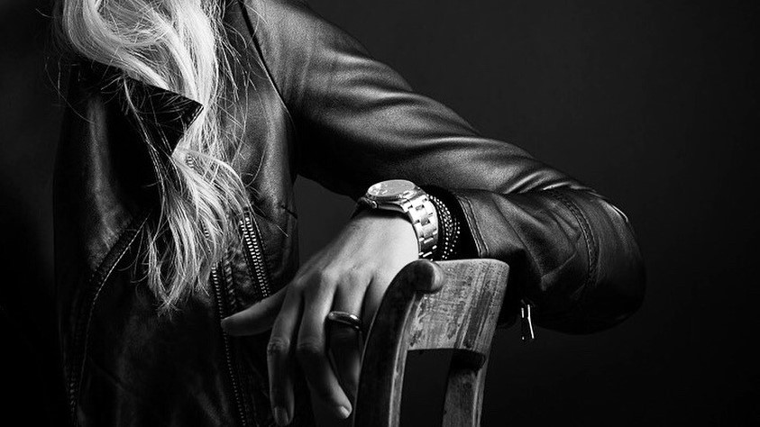 imamgine in bianco e nero di braccio di ragazza appoggiato a una sedia. al polso ha un orologio di lusso