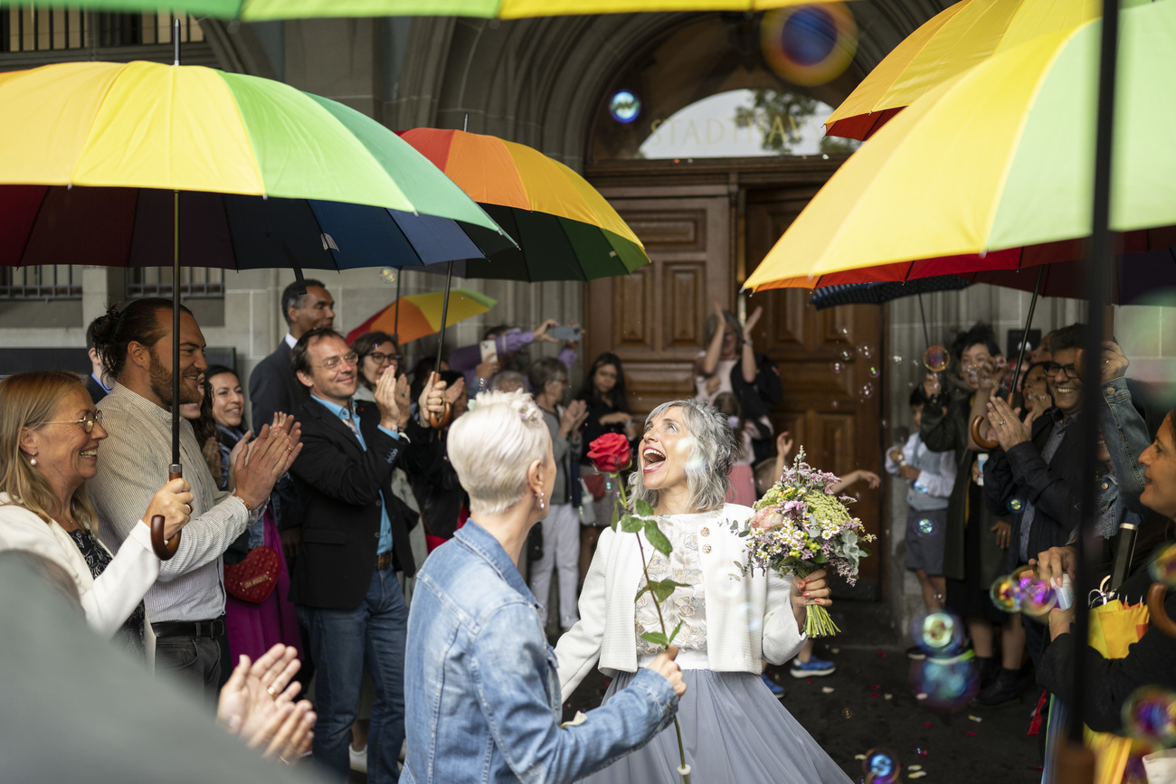 Two women greeted by umbrella holding well wishers after a marriage ceremony in Switzerland