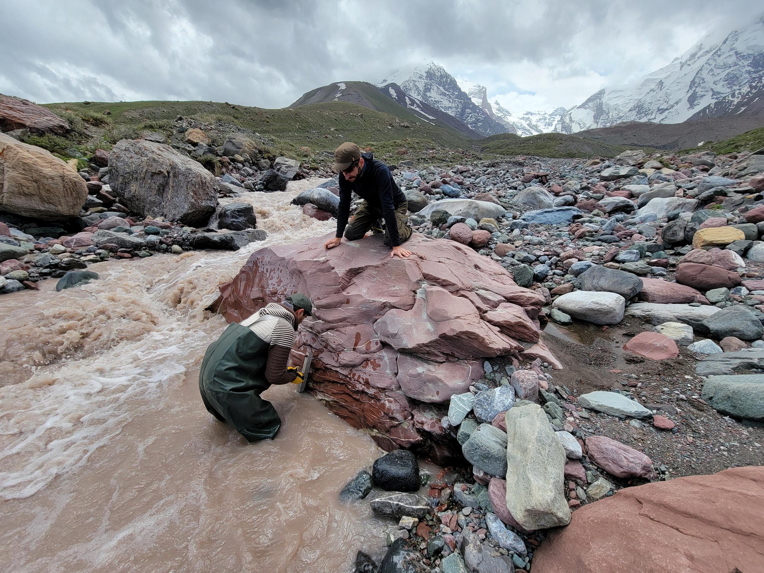 Deux personnes plaçant un appareil de mesure près d une rivière de haute montagne.