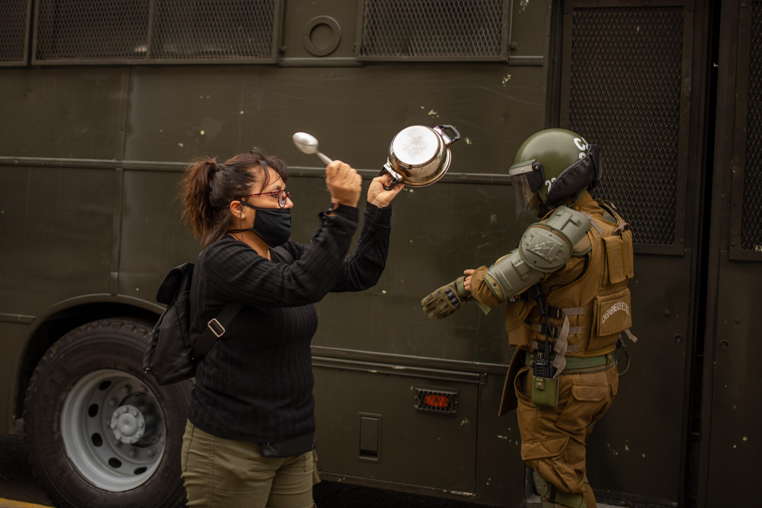 Una mujer golpea una cacerola enfrente de un policía.