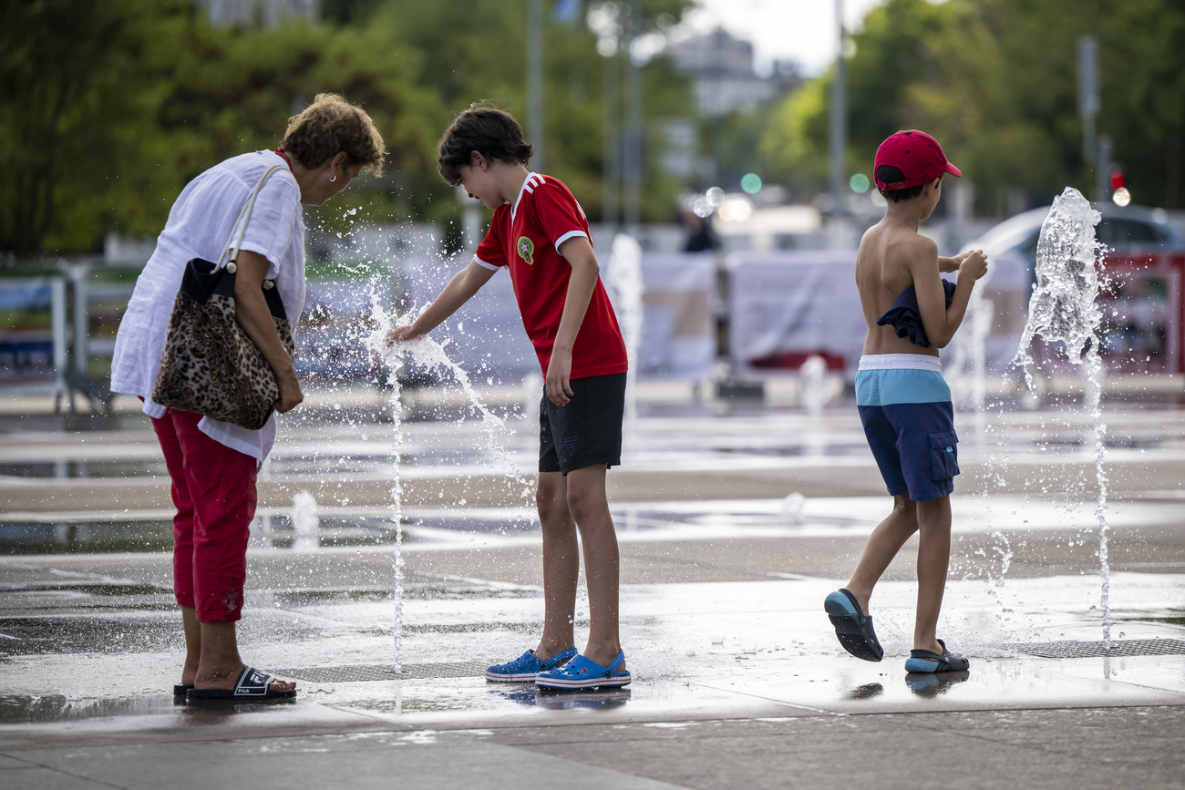 People cool off with water-jets of the fountain on the Place des Nations