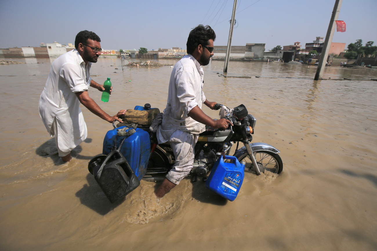 Dos hombres con una moto en zona inundada.