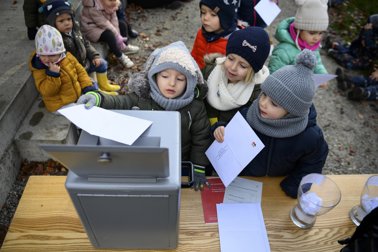 Kleine Kinder versuchen, einen Wahlzettel in eine Urne zu legen.