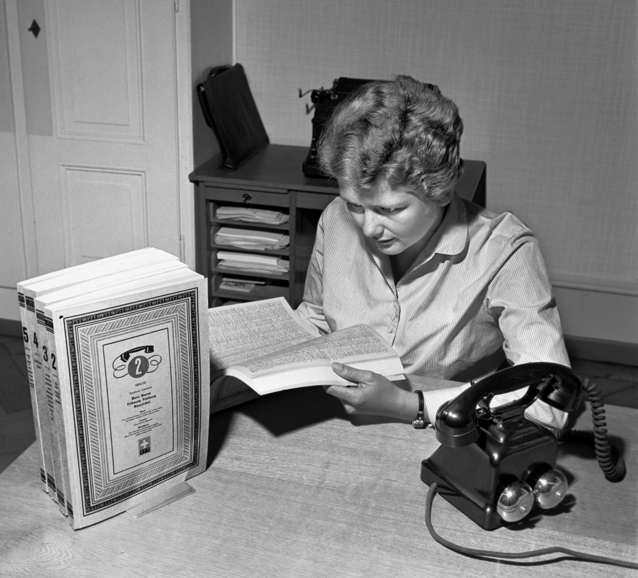 Woman reads phone directory beside a telephone