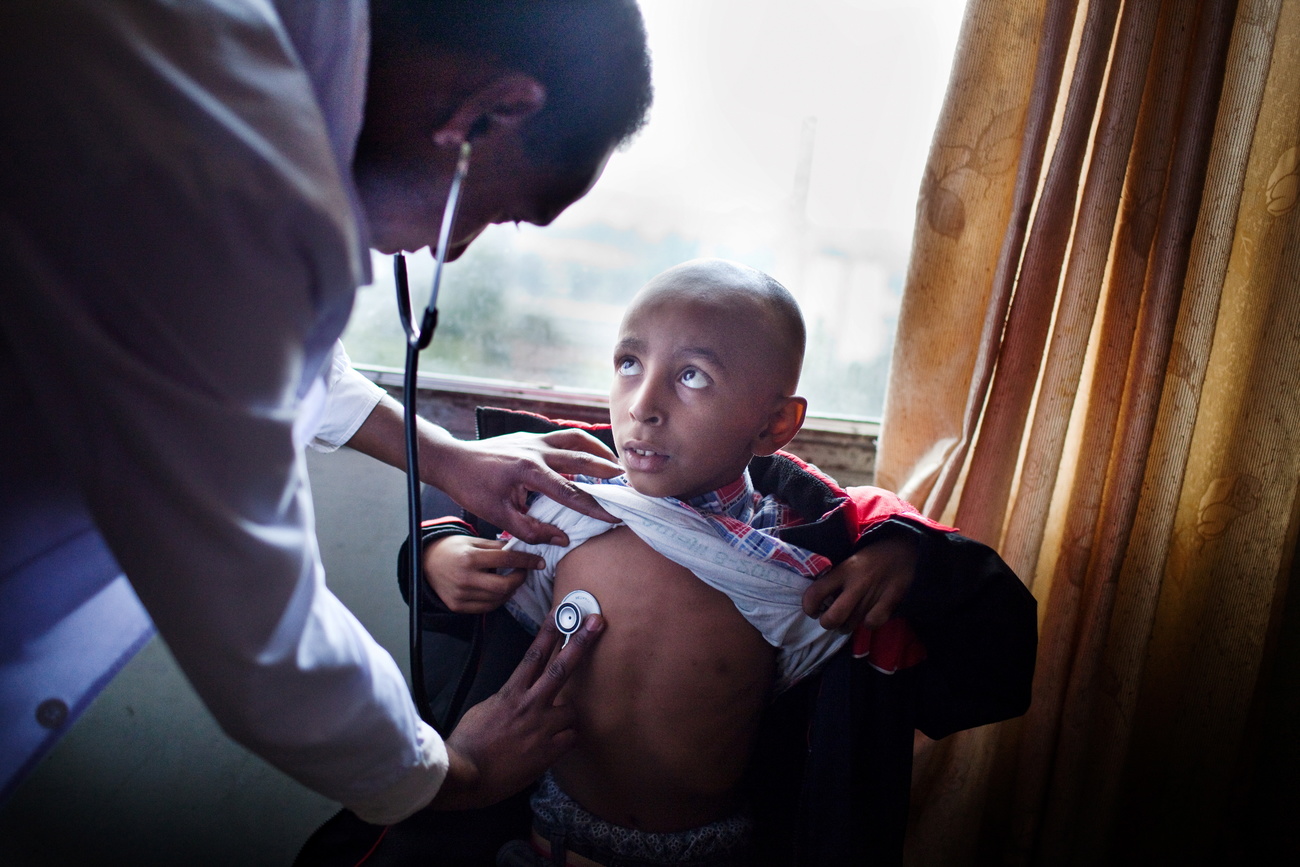 A child sits looking up at a doctor who is examining them.