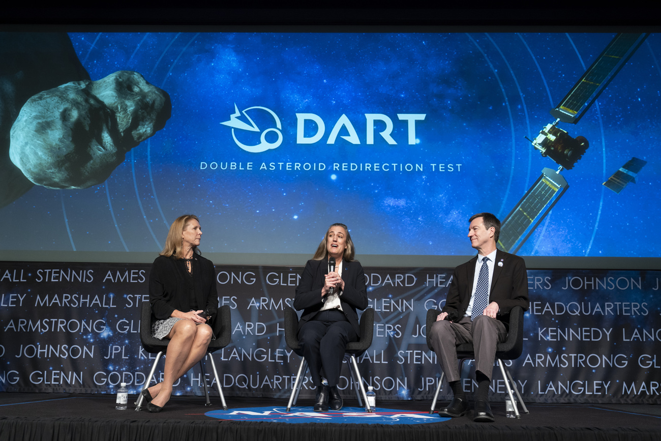 tre persone sedute dietro di loro uno schermo con nomi di astronauri e la scritta DART