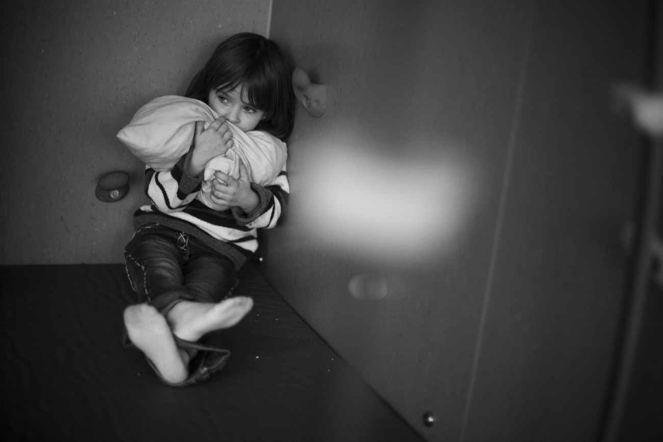 imamgine in bianco e nero di bambina seduta per terra in un angolo, abbraccia un cuscino
