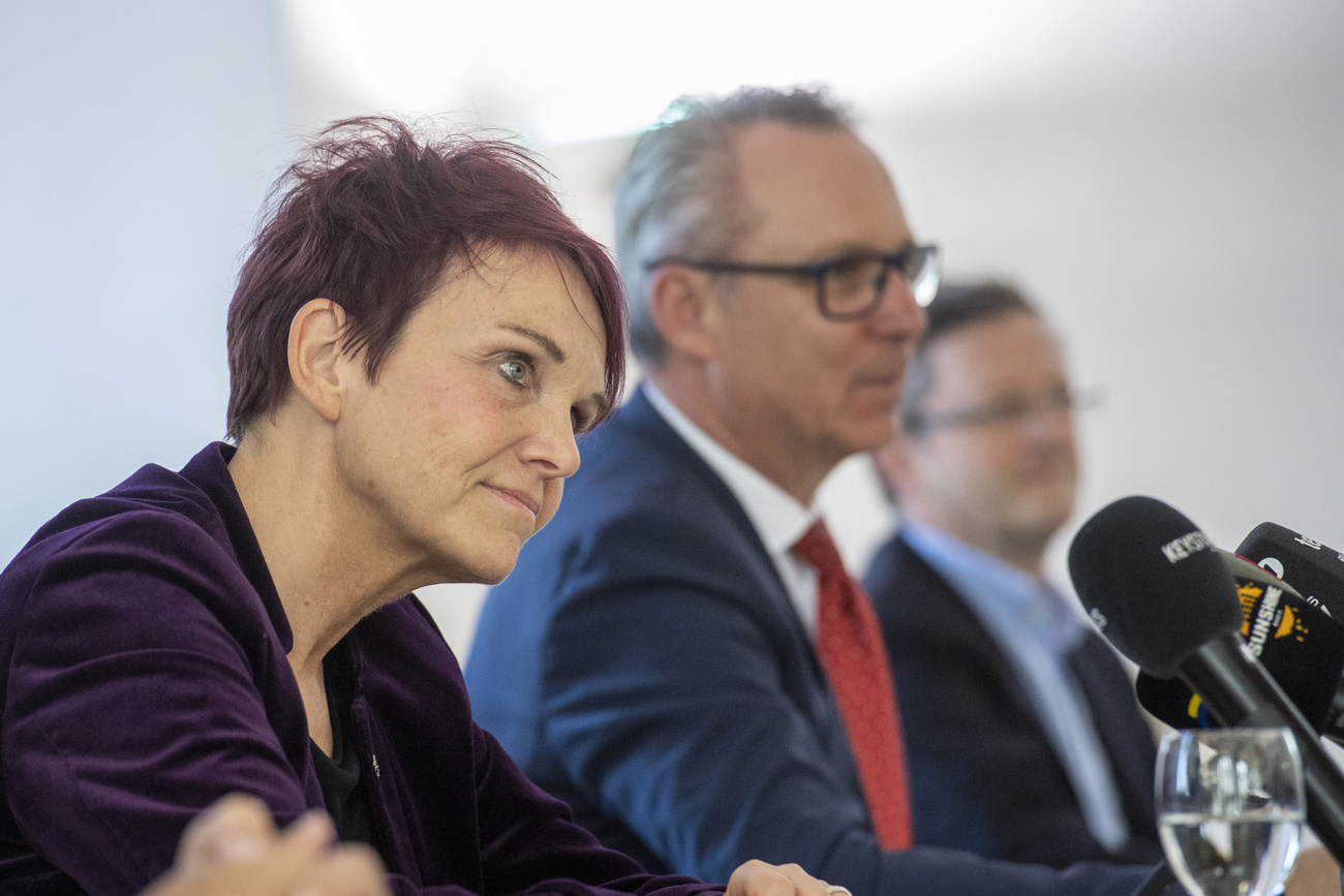 Eine Frau vor Mikrofonen, Männer im Hintergrund
