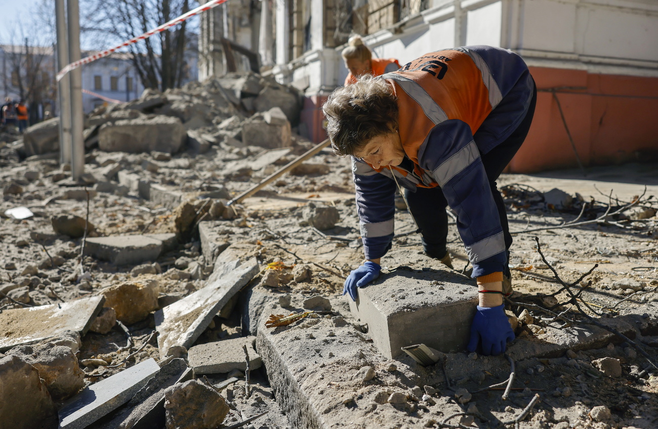 Mulher limpa escombros nas ruas da Ucrânia após explosão de uma bomba