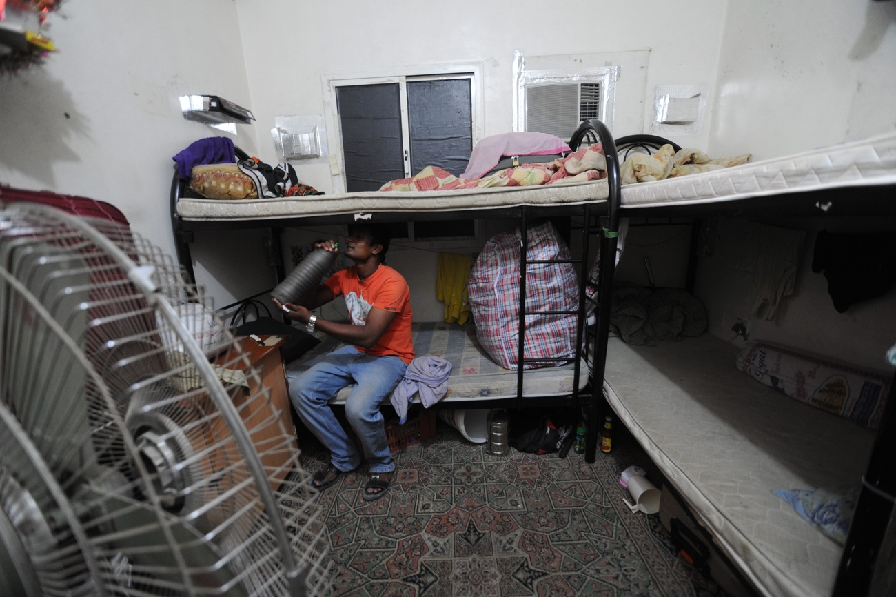 lavoratore immigrato in una stanza con letti a castello e un ventilatore