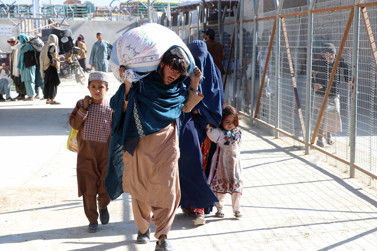 Homem afegão carrega um saco acompanhado por sua família
