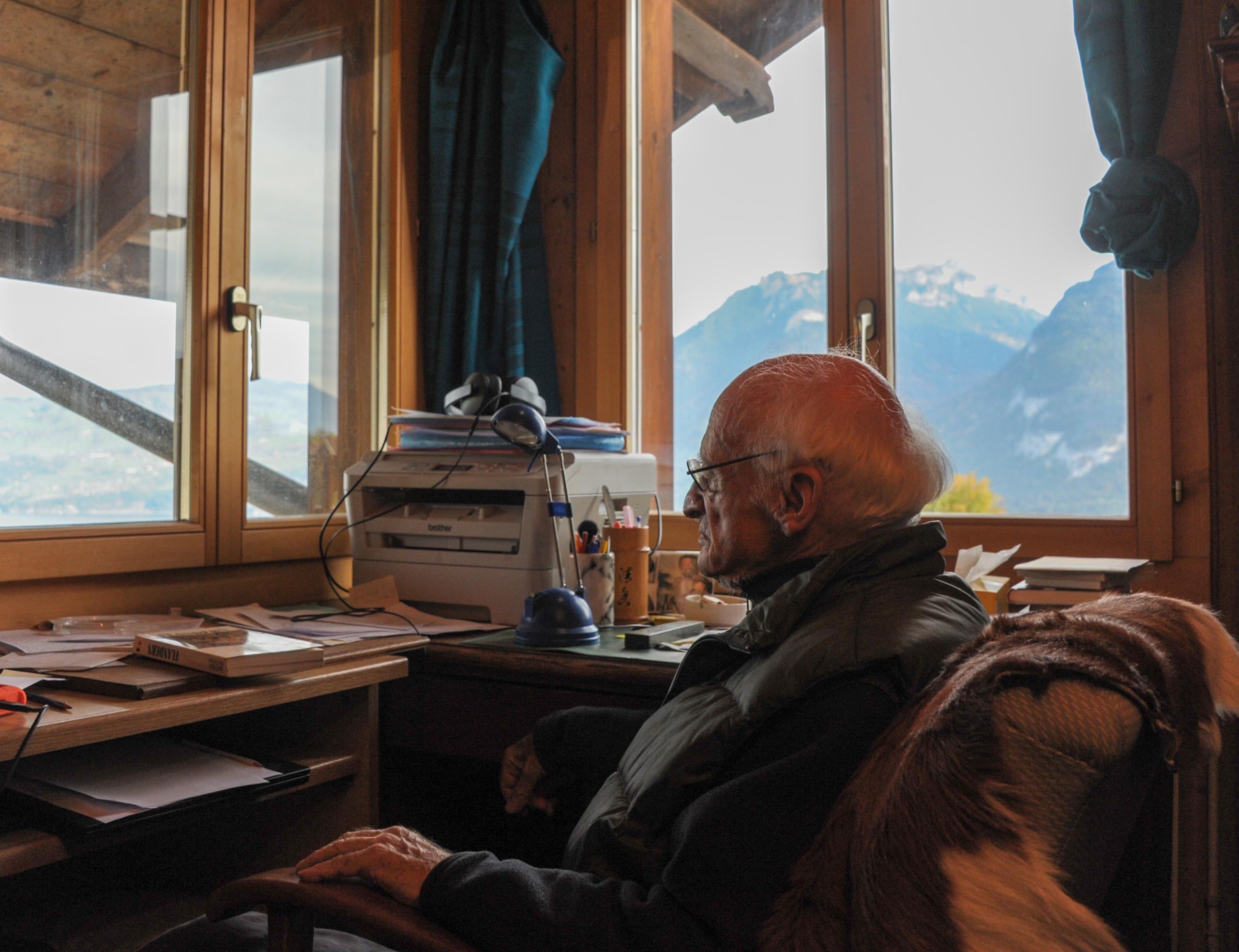 Homme âgé assis dans son chalet avec vue sur les montagnes