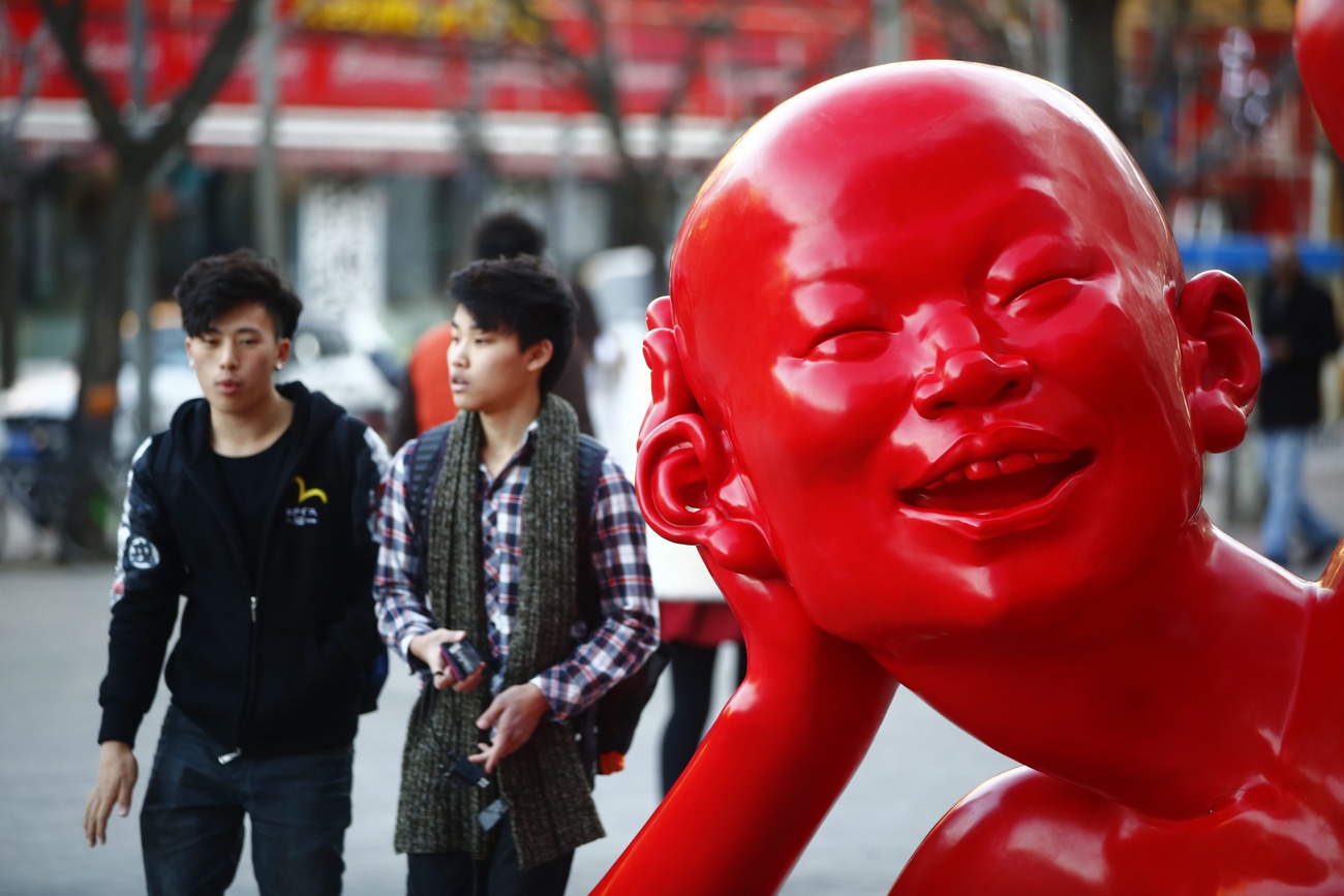 تمثال أحمر في ساحة عامة لرأس رجل يمسك بأذنه كما لو كان يُنصت إلى المارة والجمهور.