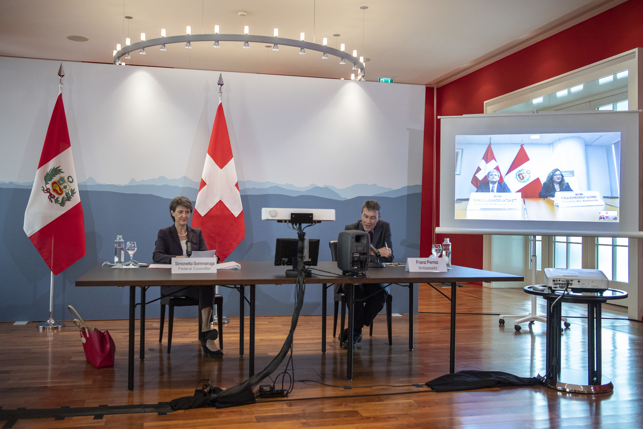 Long shot of Perrez and Sommaruga at table with flags, screen