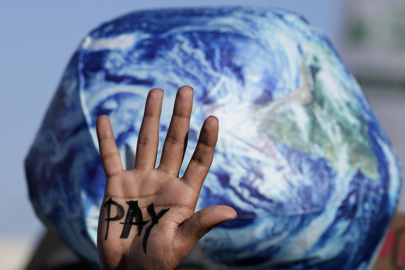 A hand reads pay calling for reparations for loss and damage at the COP27 U.N. Climate Summit,
