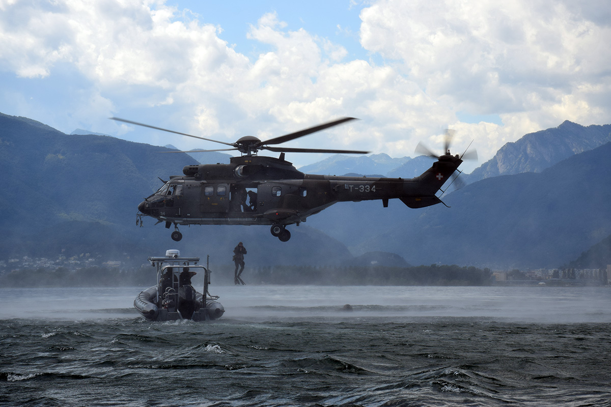 un elicottero militare vola sopra un gommone sul lago