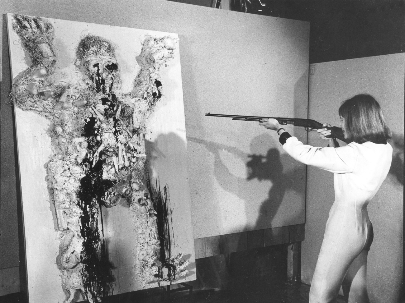 Niki apunta con un rifle a una pintura de un hombre.