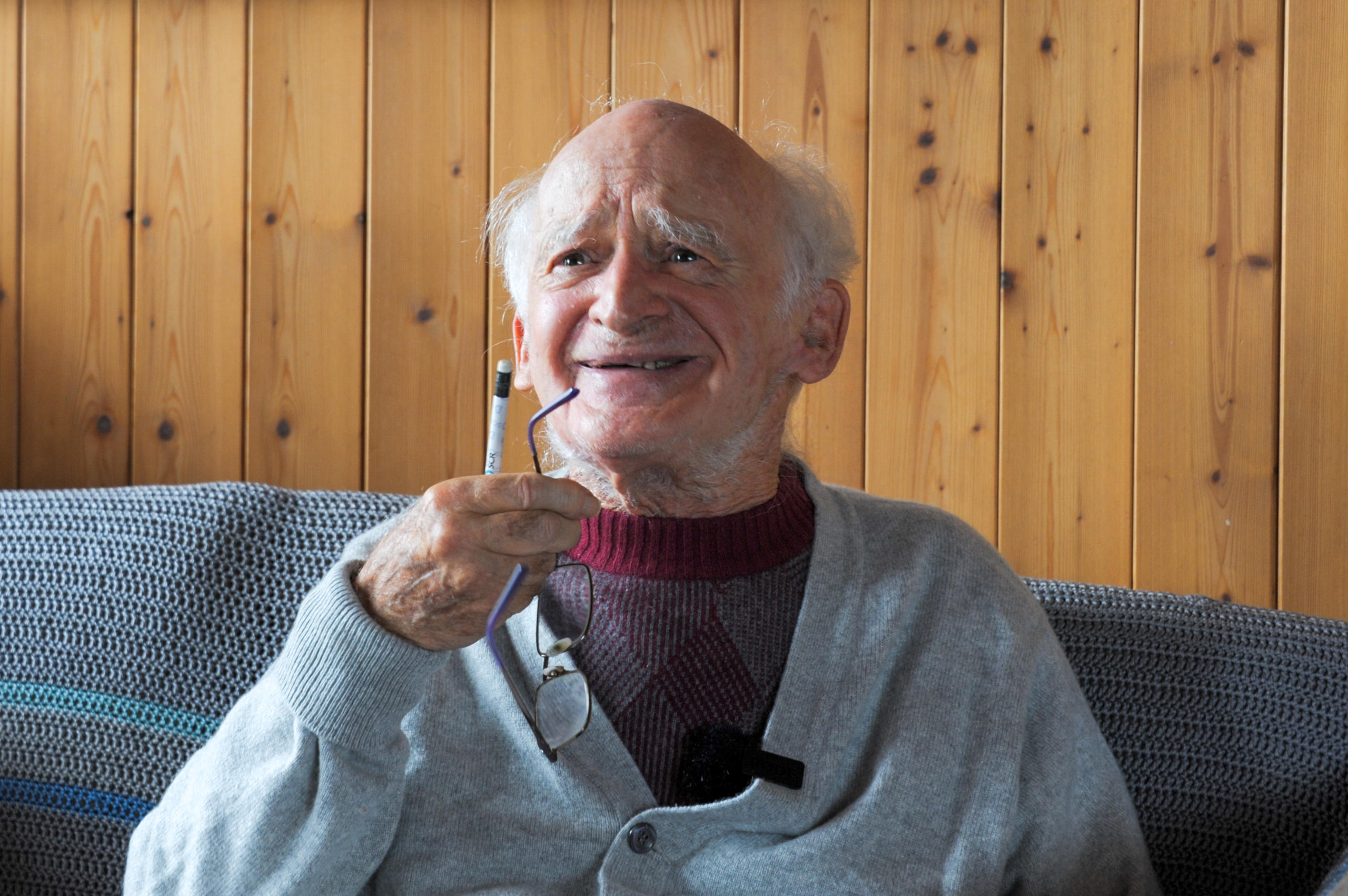 älterer Mann auf Sofa vor einer Holzwand