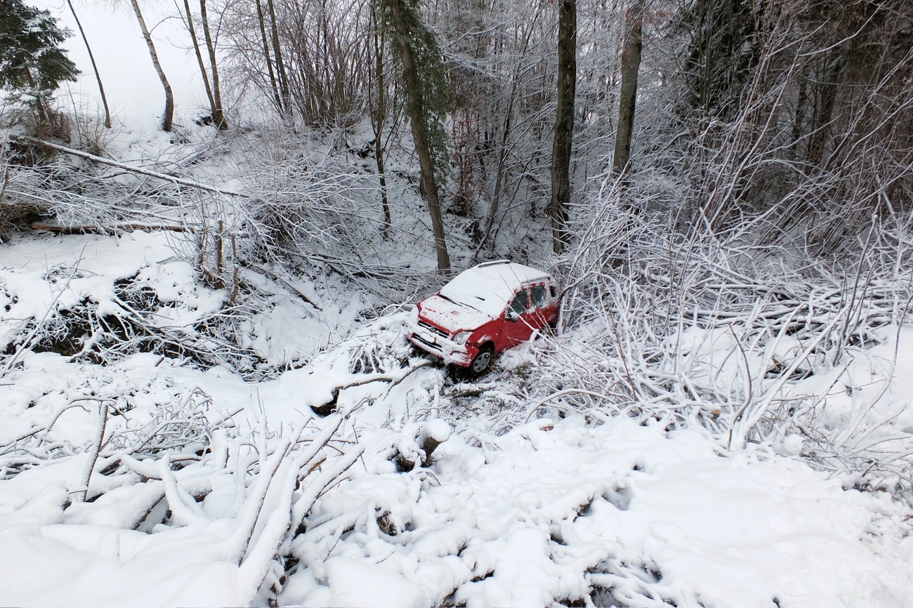 Verunfalltes Auto unten an einem verschneiten Strassenbord