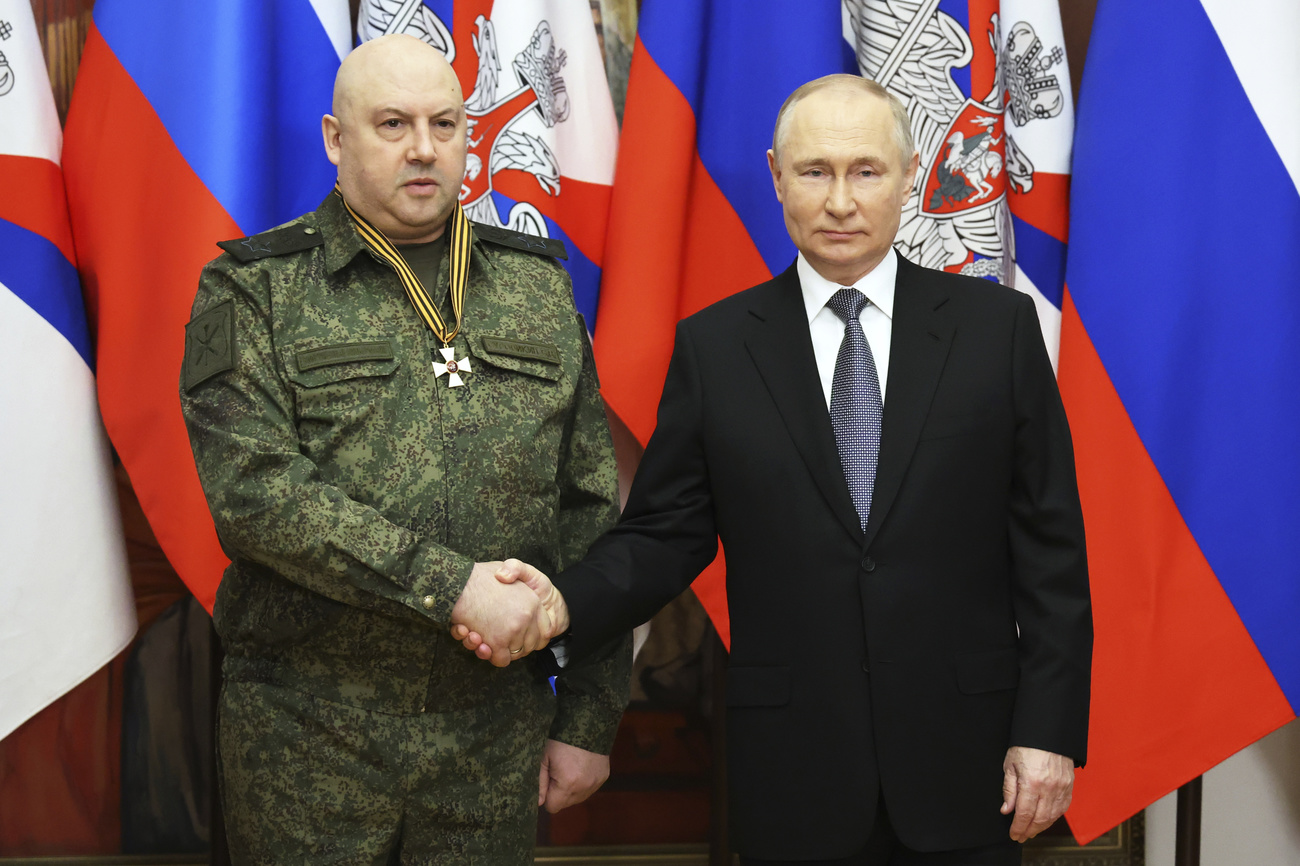 uo uono in divisa vilitare stringe la mano a un uomo in giacca e cravatta. dietro di loro bandiere russe.