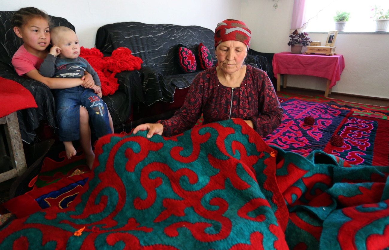 una donna sta lavorando su un tappeto di feltro mentre due bambini siedono su un divano