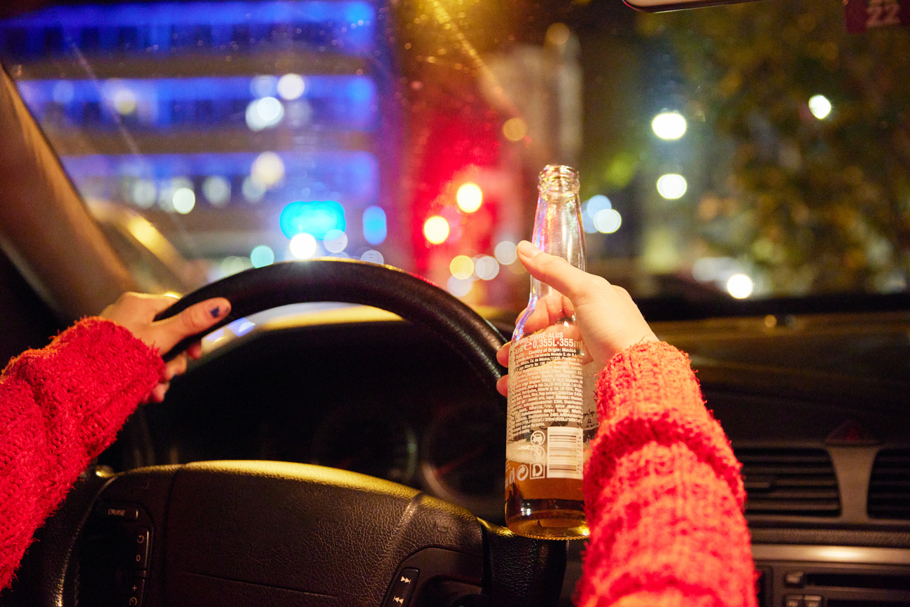 Una giovane donna al volante con una bottiglia di birra in mano.