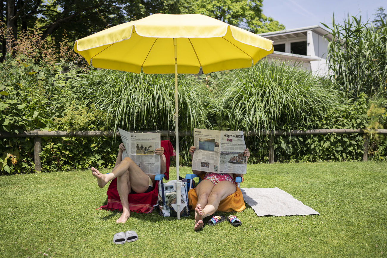 Personas leyendo el periódico bajo una sombrilla en un jardín.