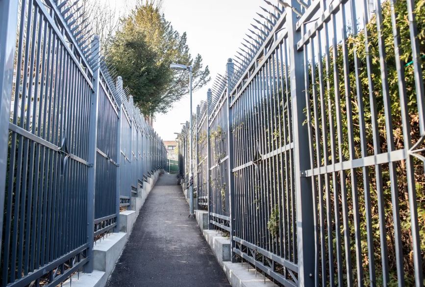Enger Gehweg mit hohen Zäunen auf beiden Seiten